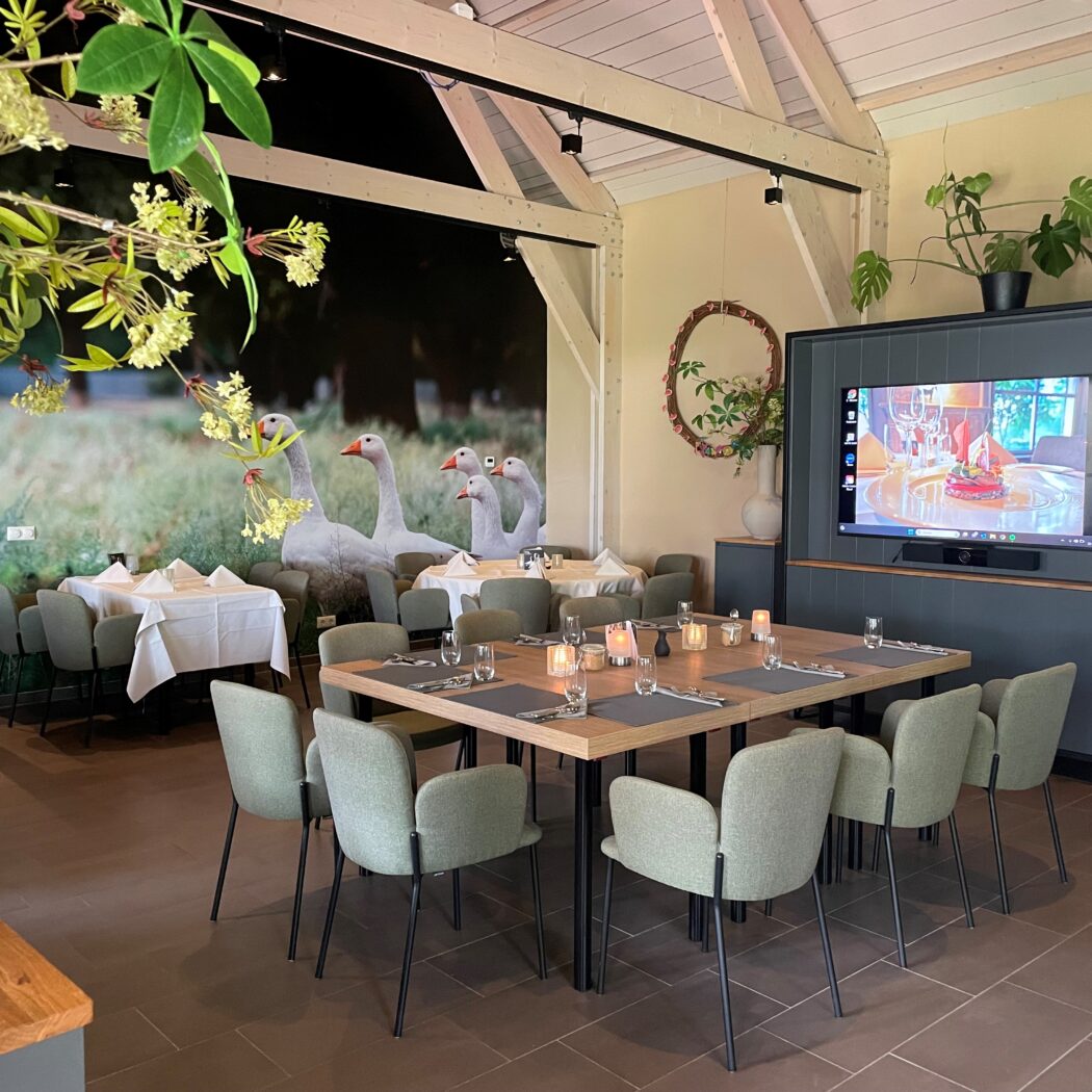 Ruim restaurant of evenementenlocatie met gedekte tafels, een muurschildering van ganzen en een tv-scherm.