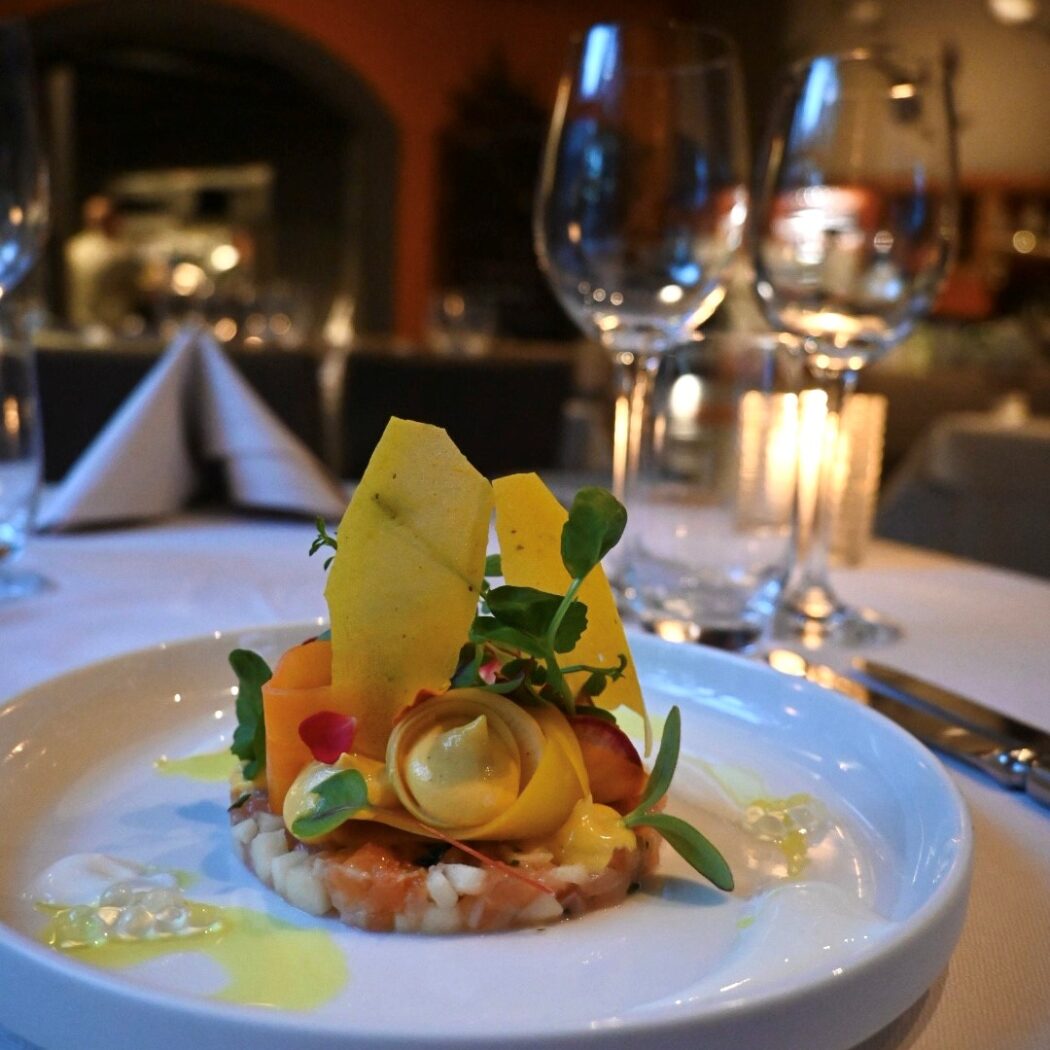 Culinair gerecht op wit bord met fijngehakte basis, gele pasta met crème en verse kruiden in restaurant.
